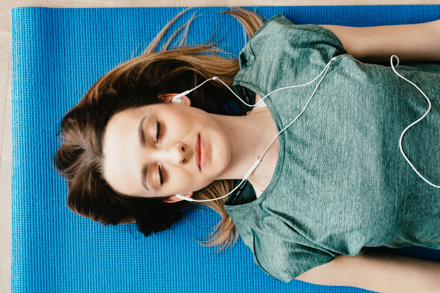 安静的女人在家里戴着耳机，面朝上躺在瑜伽垫上休息